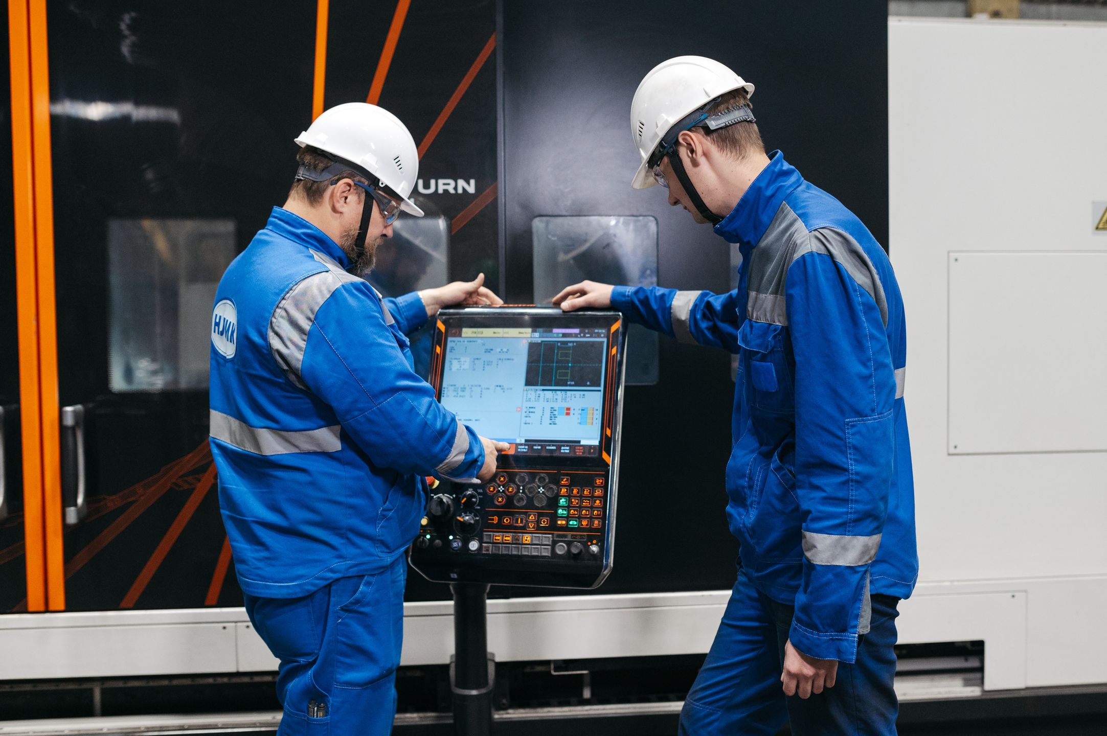 Two engineers operating CNC machinery in a factory