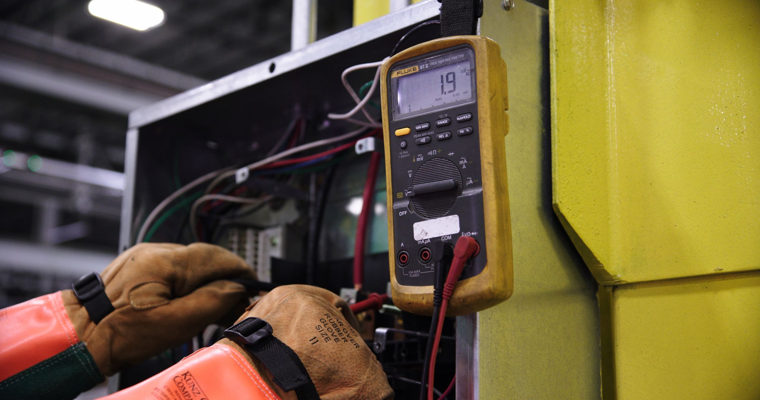 Electrician using a multimeter on industrial control panel wiring
